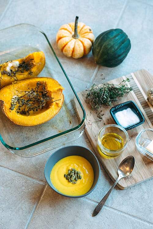 spices, herbs, garlic, butter, pumpkin halves and cooked pumpkin in pan on a counter top