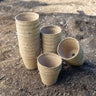 Round tan peat pots stacked neatly in four rows in a garden bed.