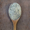 White garlic pepper, flecked with black and green inclusions, on a rustic wooden spoon.